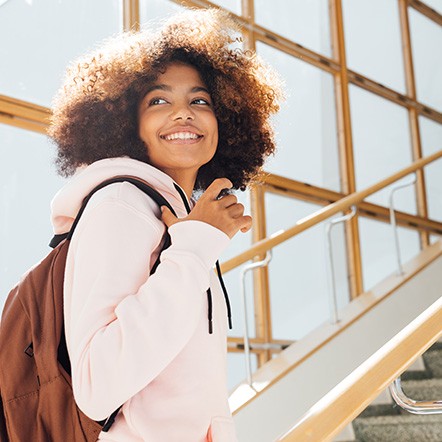 Teen girl with backpack smiling while walking up stairs