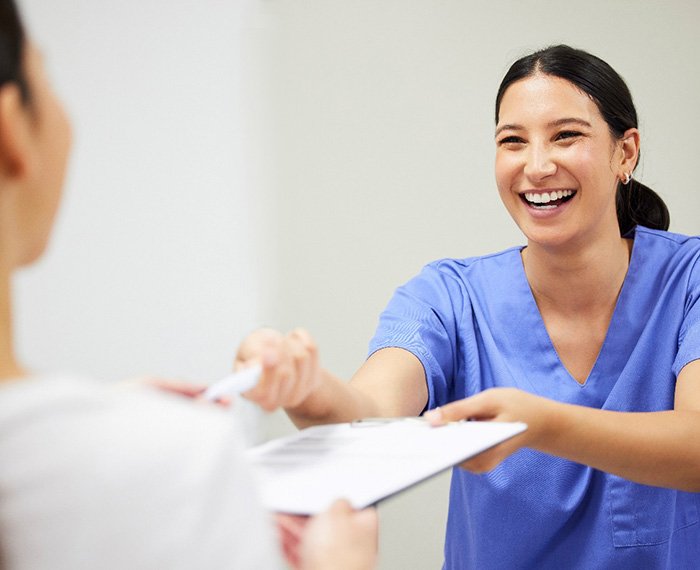 Dental assistant smiling while handing patient form