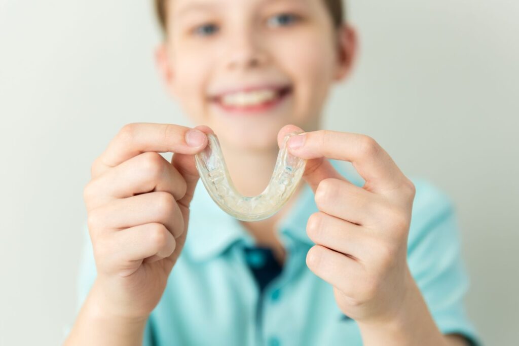 A boy holding his Invisalign aligner and smiling.