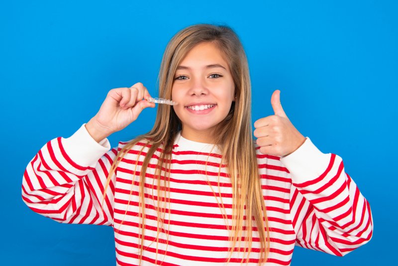 A teen girl wearing a striped shirt holding an Invisalign aligner